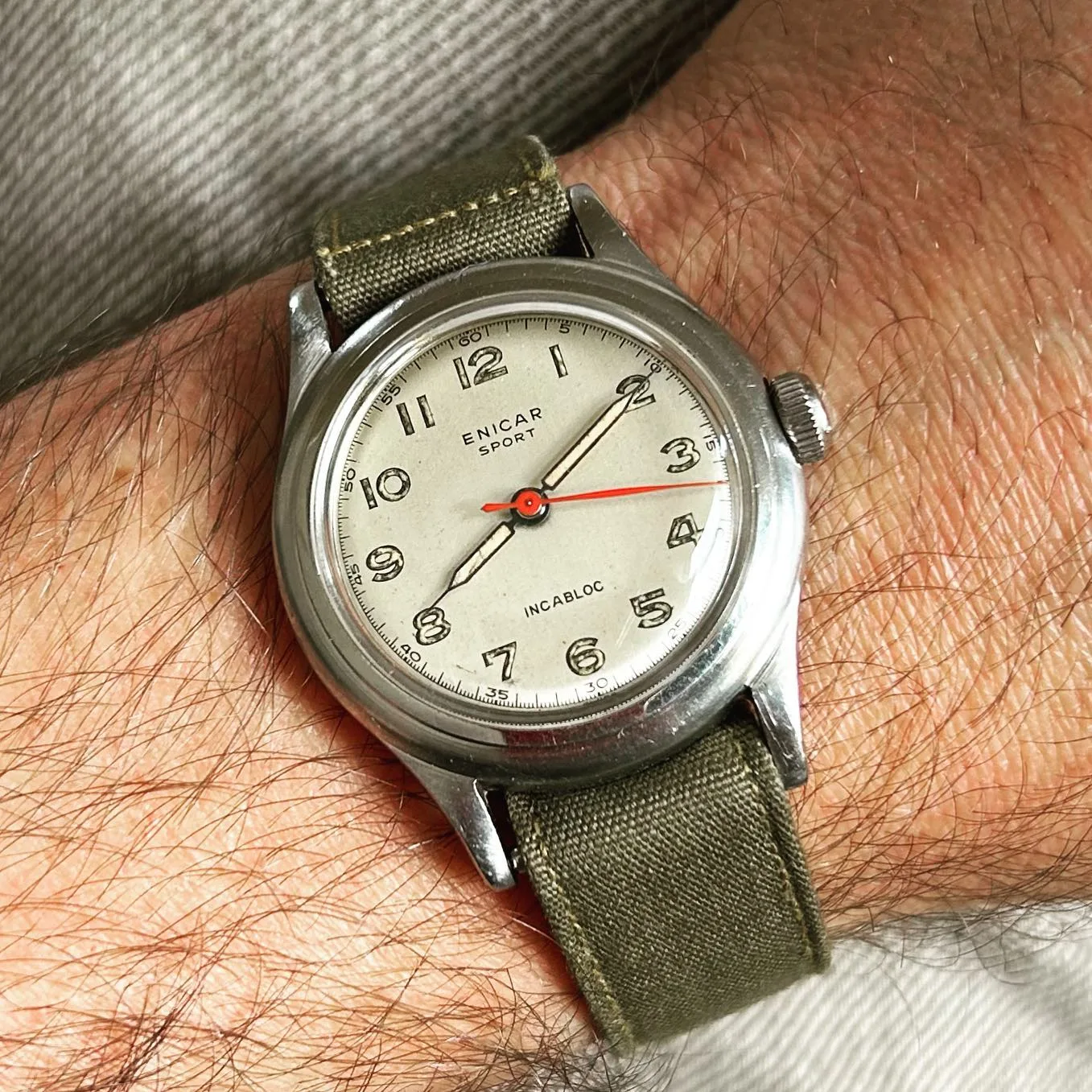Enicar Sport with a white dial, Arabic numerals and red centre seconds on an olive canvas strap, on the wrist