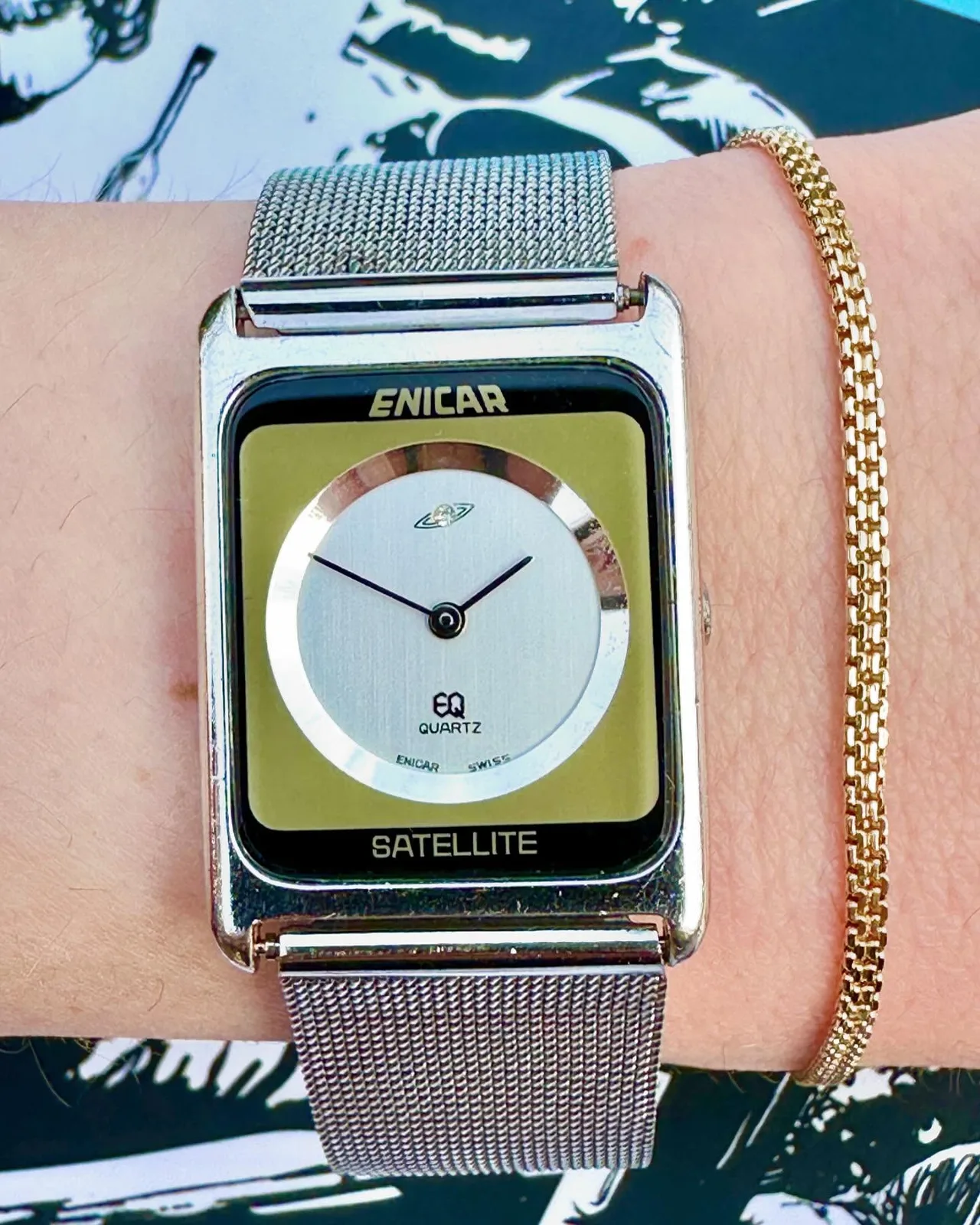 EQ Quartz Satellite with a silver dial and gold-coloured surround in a rectangular silver-coloured case on a mesh bracelet, on the wrist
