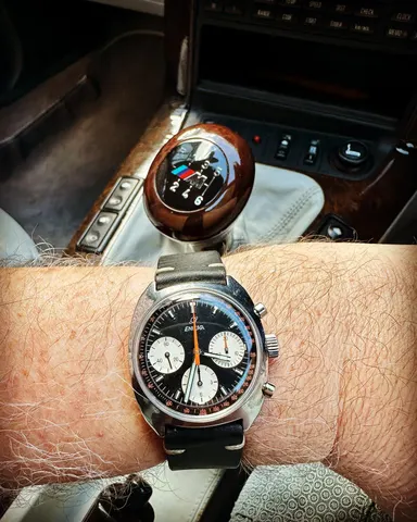 Gerhard Mitter chronograph with a black dial and white registers on the wrist, by the gear lever of a car