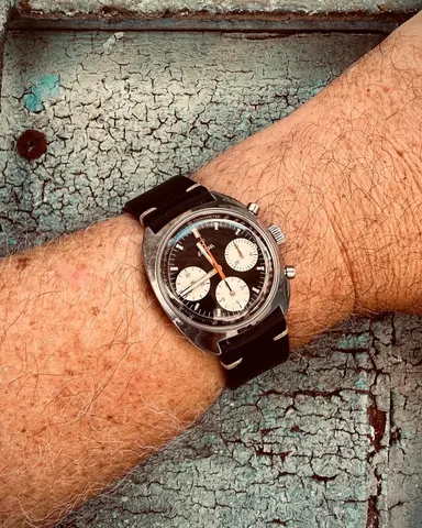 Gerhard Mitter chronograph with a black dial, white registers and orange chronograph hand in a cushion case, on the wrist against a cracked painted door