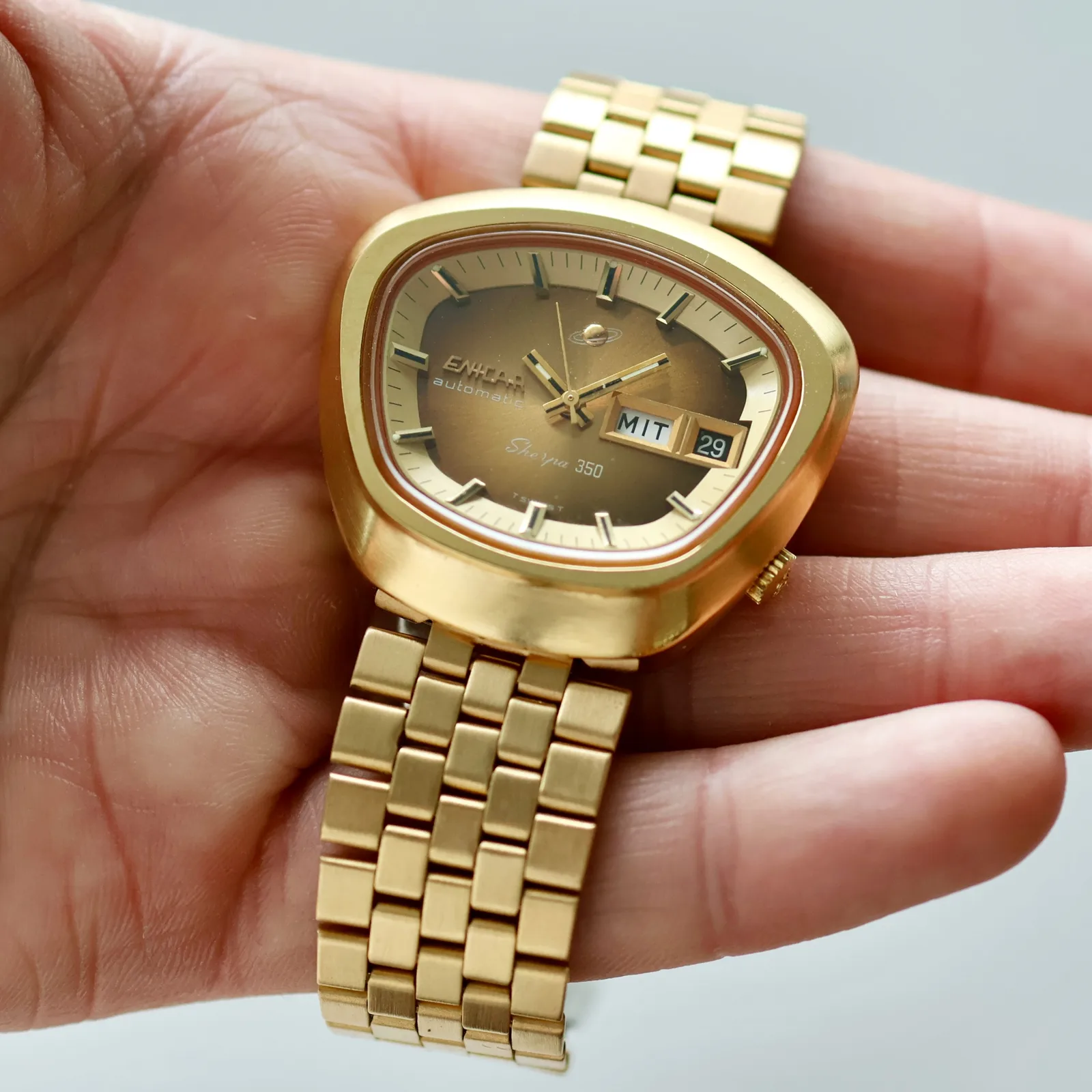 Gold-plated Sherpa 350 with a brown gradient dial and day-date in a trapezium case, on its gold bracelet in the hand
