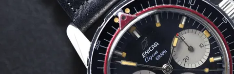 Close-up of an Aqua Graph bezel at 12 with the red ring's triangle pointer, black dial with grey registers