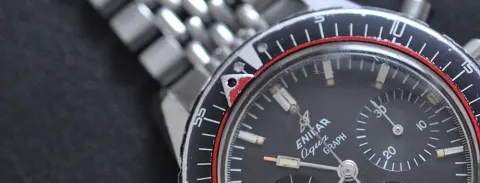 Close-up of an Aqua Graph bezel at 12 with the red ring's triangle pointer and two lume spots, black dial