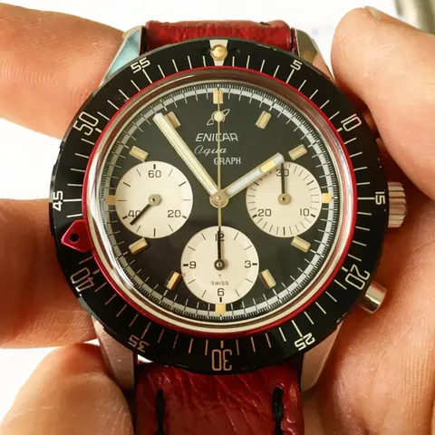 Aqua Graph with a black racing dial and white registers on a red strap, held in the hand