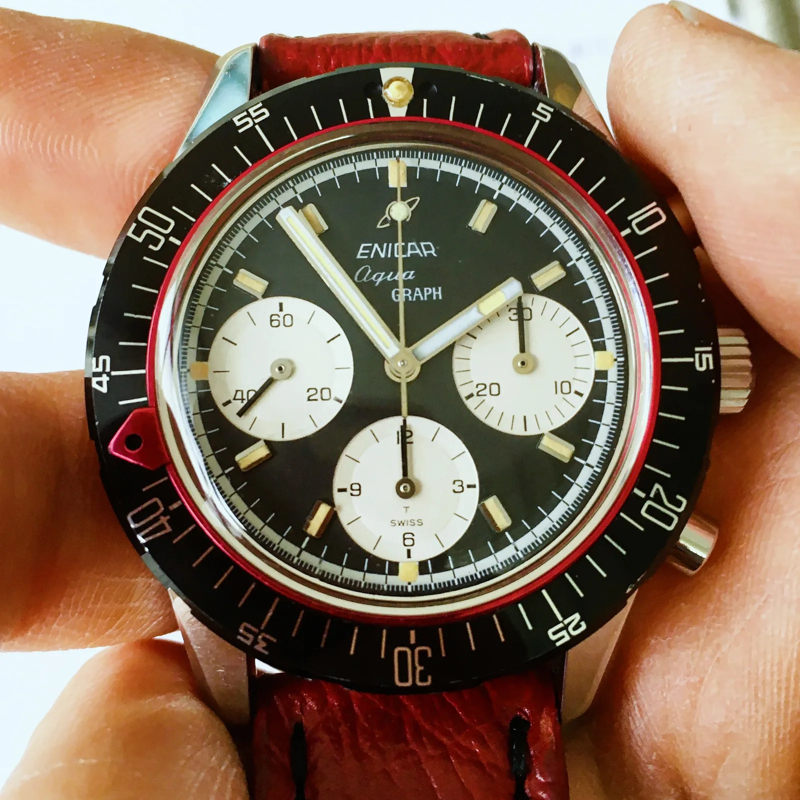 Aqua Graph with a black racing dial, white registers and black outer bezel with red pointer, held in the hand
