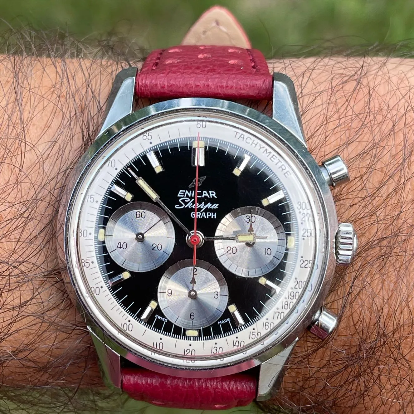 Sherpa Graph with a black dial, silver registers and white Tachymetre ring on a red strap, on the wrist