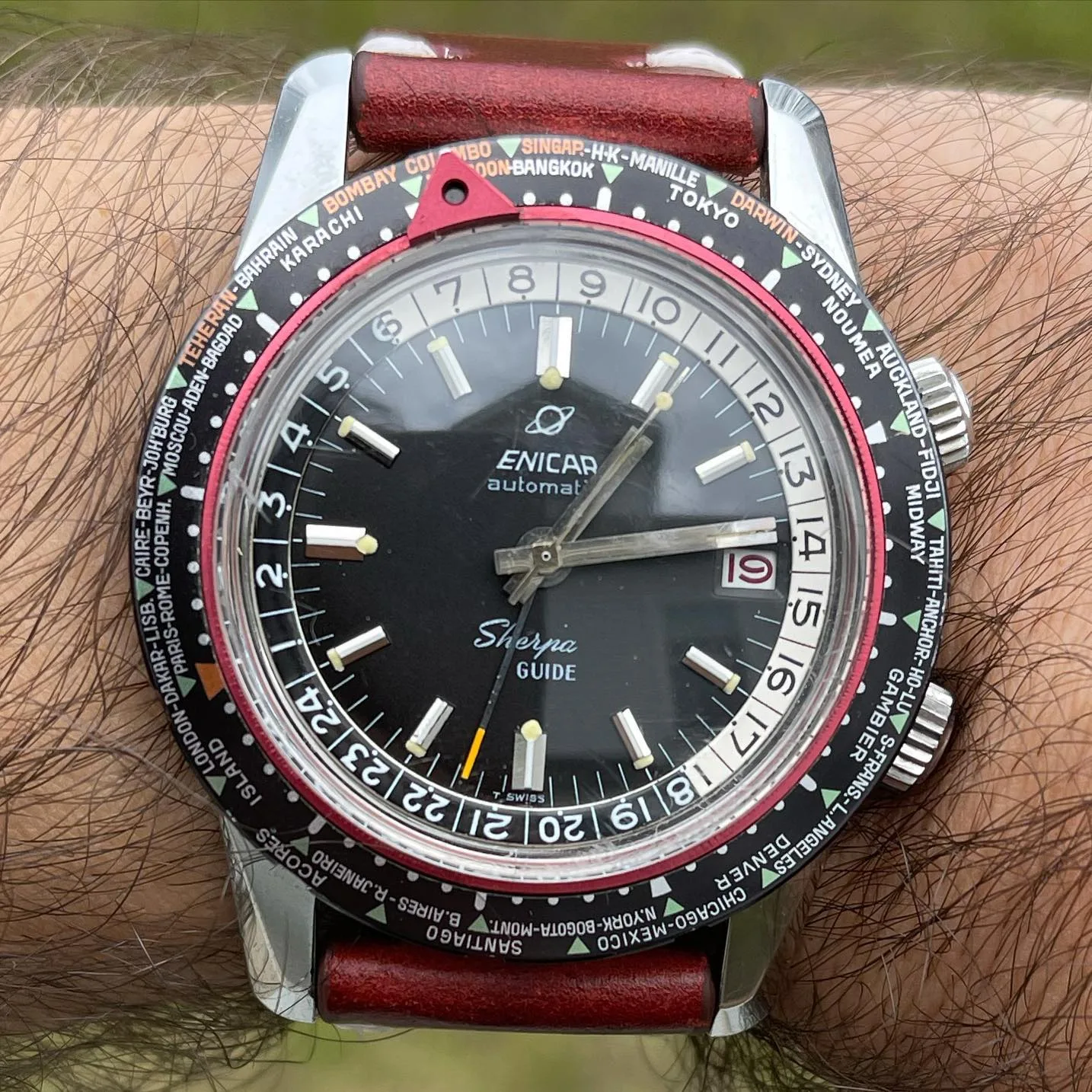 Sherpa Guide with a black dial, world-city bezel and red pointer on a red strap, on the wrist
