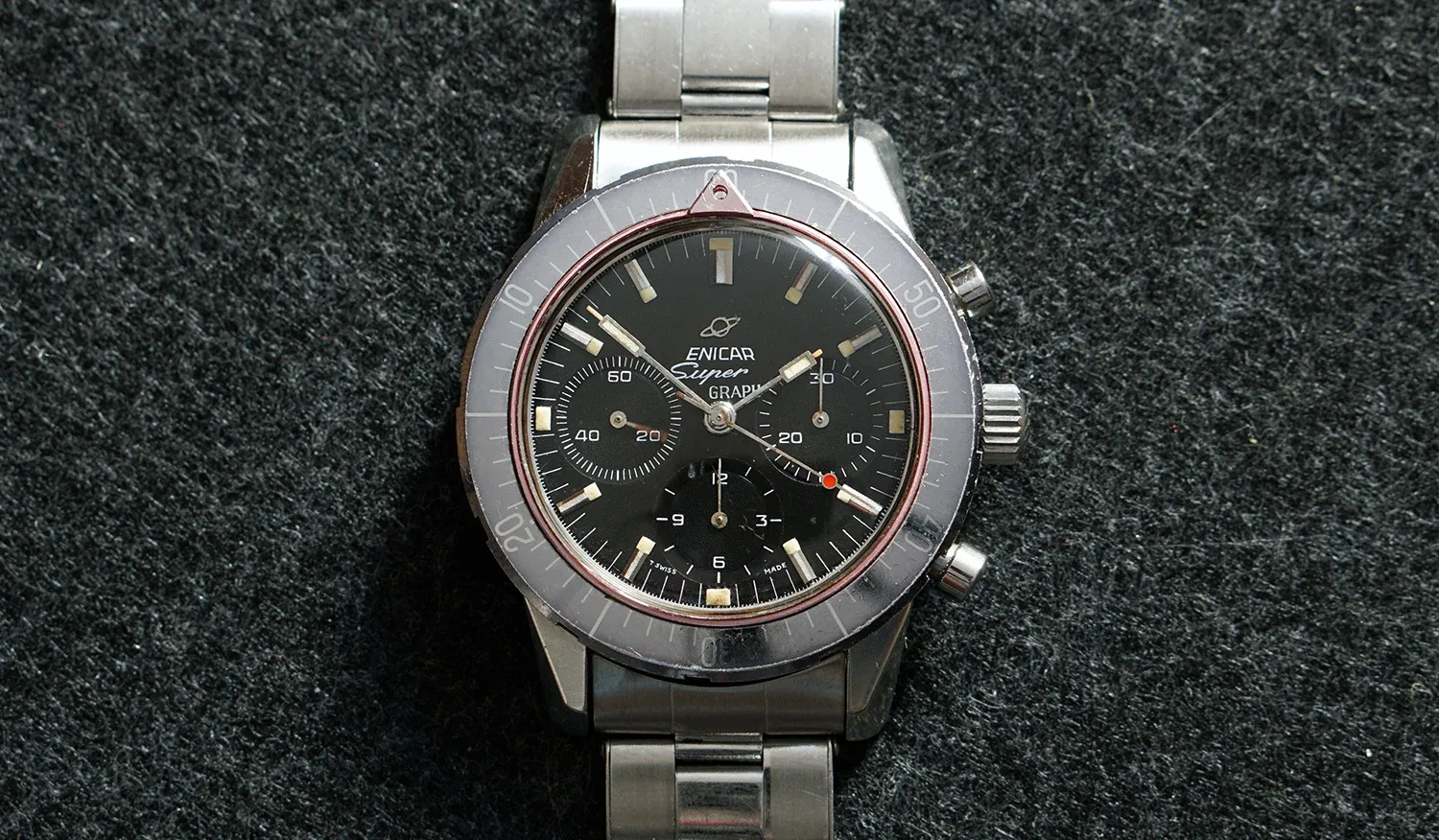 Super Graph with an all-black dial, grey countdown bezel and red ring, on a steel bracelet