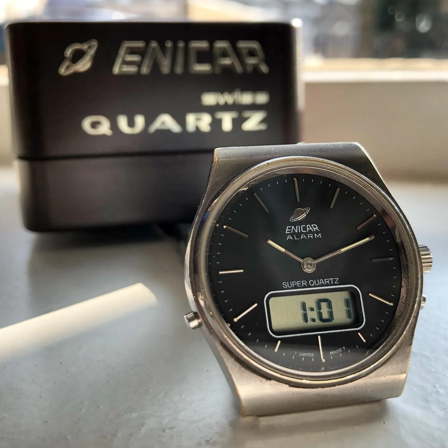 Super Quartz Alarm with a black dial and an LCD window below the hands, in front of its box