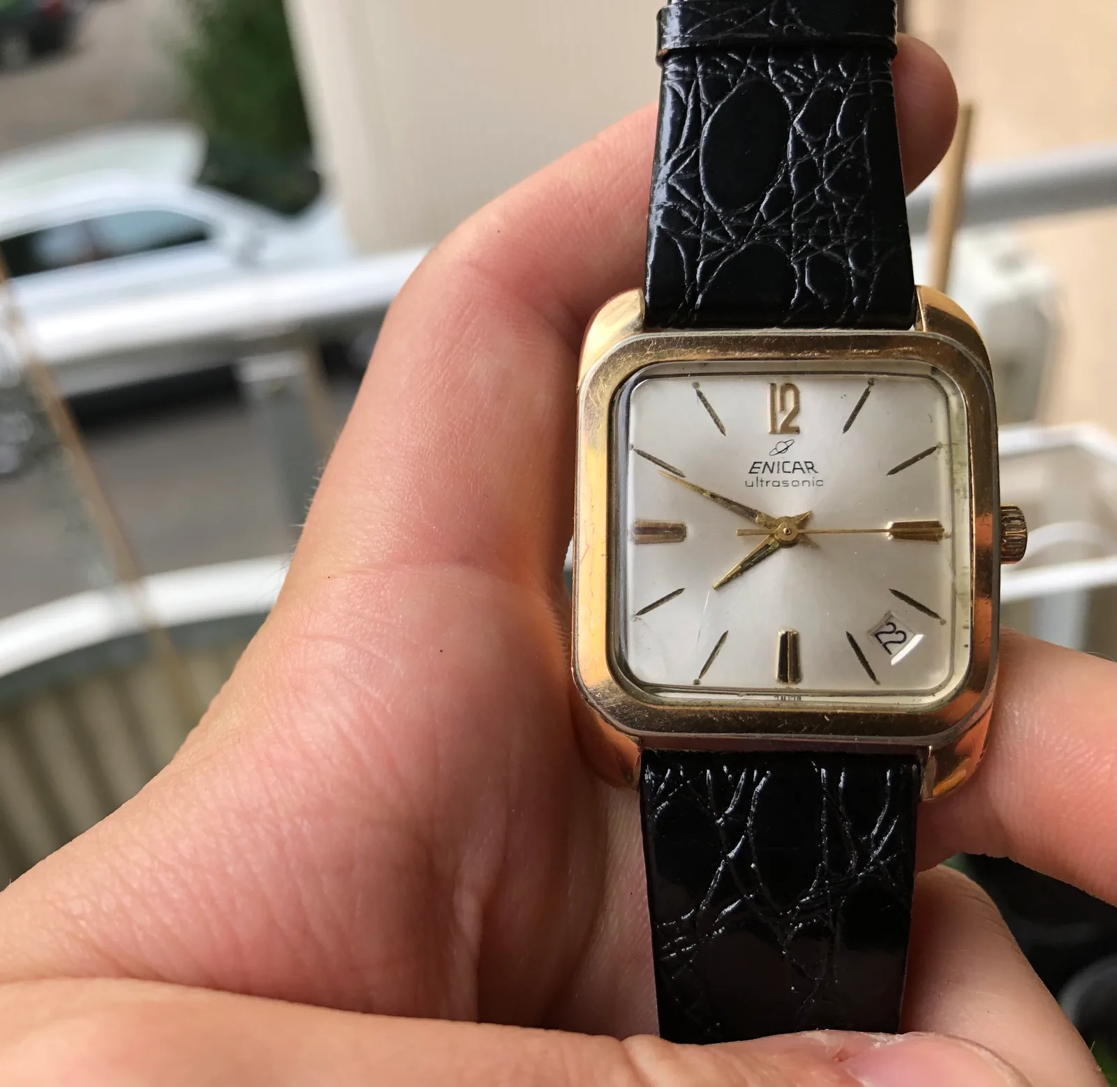 Gold-plated Enicar Ultrasonic with a square case, silver dial, gold baton markers and a date window, held in a hand